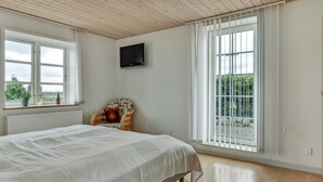 A bedroom with a large bed, a television on the wall, and a window with a view of greenery.