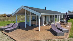 A modern house with a covered patio area featuring lounge chairs and a dining table.