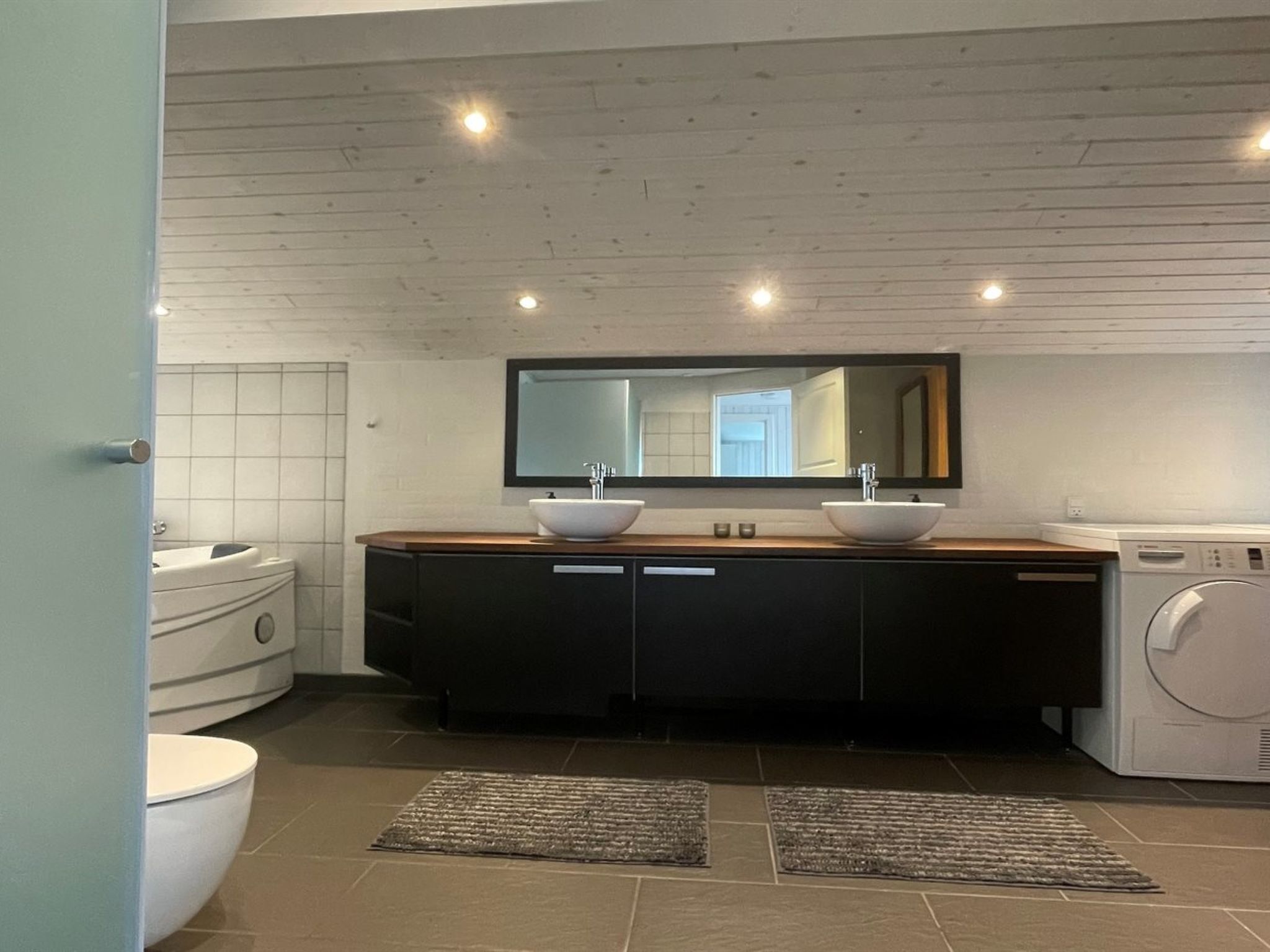 Une salle de bain moderne avec deux lavabos, un grand miroir, un lave-linge et des toilettes.
