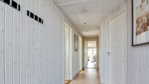 A hallway with white wooden walls, a dark bench, and a rug leading to a door.