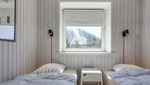 A small, well-lit room with two beds, a small table, and a window providing a view of trees outside.