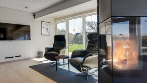 A modern living room with a fireplace, two leather chairs, a coffee table, and a TV mounted on the wall.