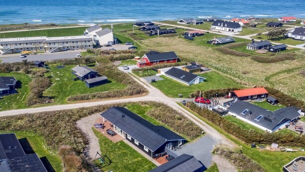 An aerial view of a coastal residential area with houses, a road, and a beach.