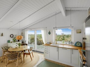 A modern kitchen with a large window, white cabinetry, and a dining area with wicker chairs.