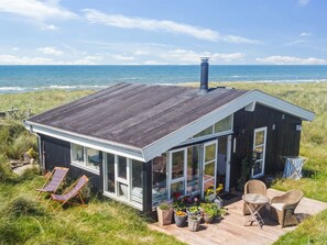 Une maison de plage moderne dotée d’une grande baie vitrée, d’une terrasse et de mobilier d’extérieur.