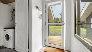 Un lavadero con lavadora, una puerta que da a una terraza exterior y vistas a una zona verde.