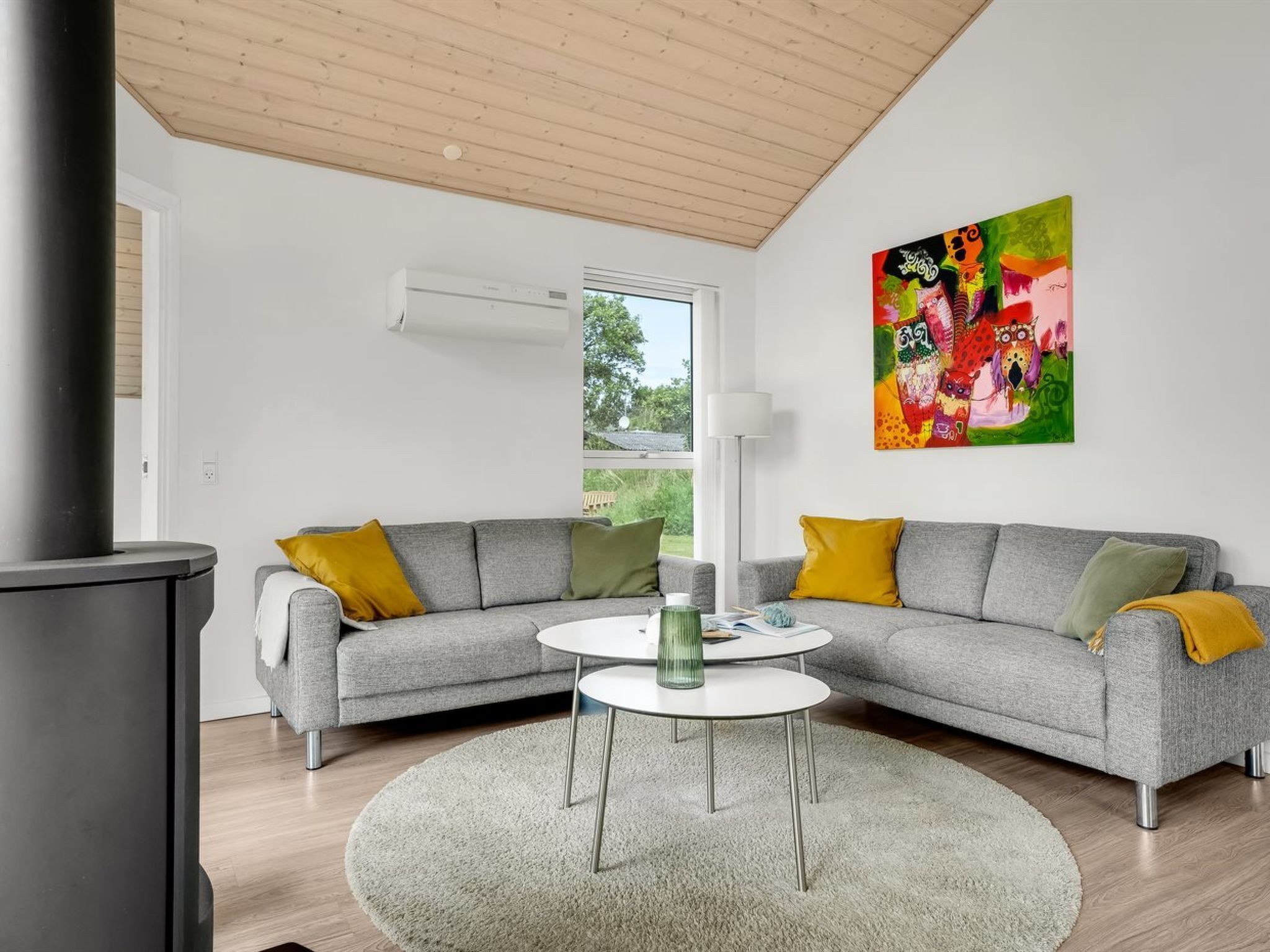 A modern living room with a grey sectional sofa, a round coffee table, and a colorful abstract painting on the wall.
