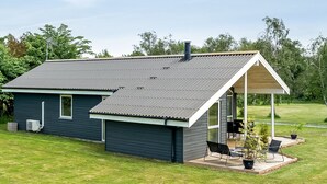 Una casa moderna con techo de metal gris, un porche cubierto con mobiliario exterior y un césped bien cuidado.