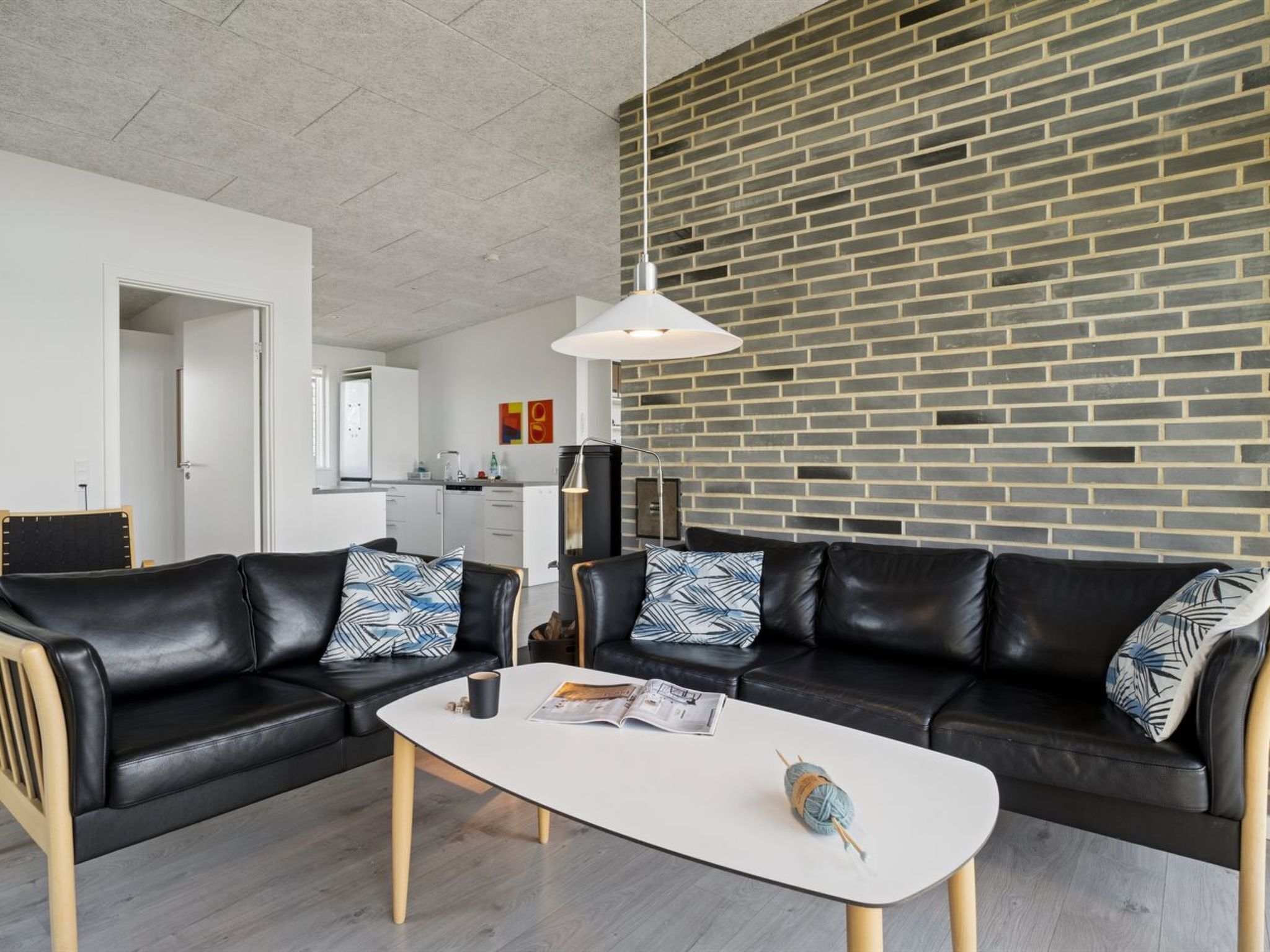 Een moderne woonkamer met twee zwarte leren banken, een witte salontafel en een muur met een bakstenen patroon.