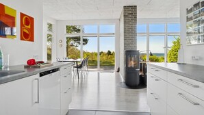 Una cocina moderna con armarios blancos, una isla central y un amplio ventanal con vistas a zonas verdes.
