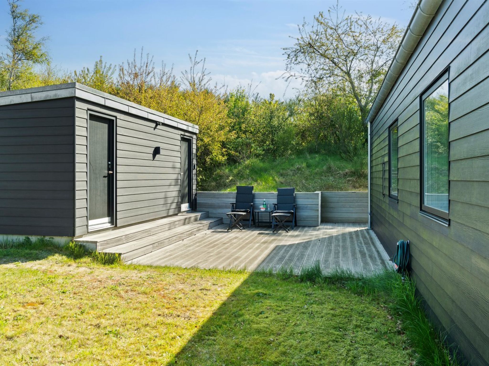 A modern outdoor patio with a wooden deck, a small table, and two chairs.