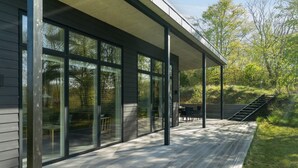 Una casa moderna con amplios ventanales, un porche cubierto y una terraza de madera.