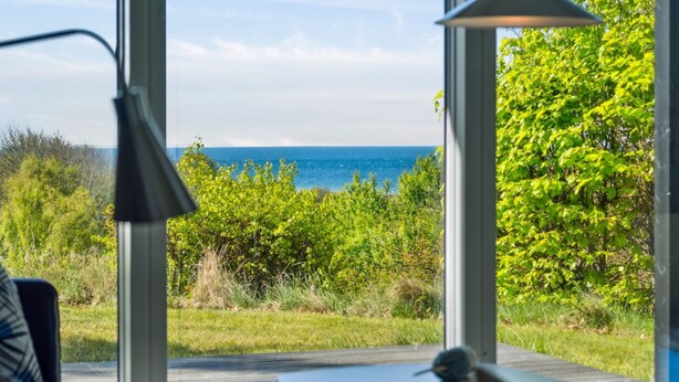 Una habitación con vistas al océano a través de amplios ventanales, un escritorio con una lámpara y un pájaro en el escritorio.