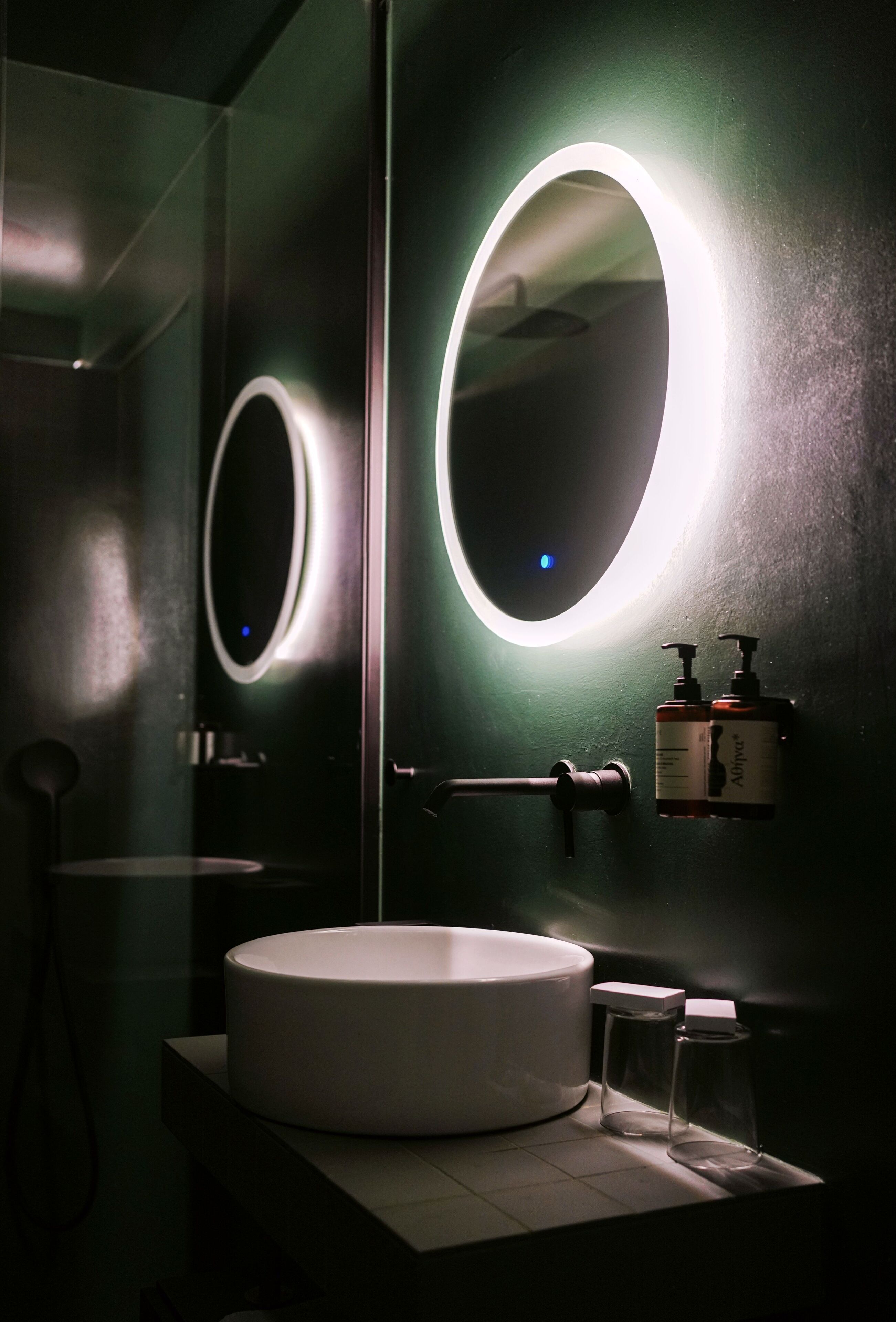 A modern bathroom with a round mirror, a white sink, and two bottles of hand soap.