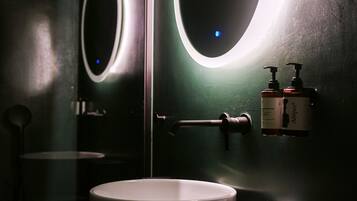 A modern bathroom with a round mirror, a white sink, and two bottles of hand soap.