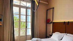 Ein Hotelzimmer mit Bett, einem Vorhangfenster, einem Kopfteil und einem Regal mit Büchern.