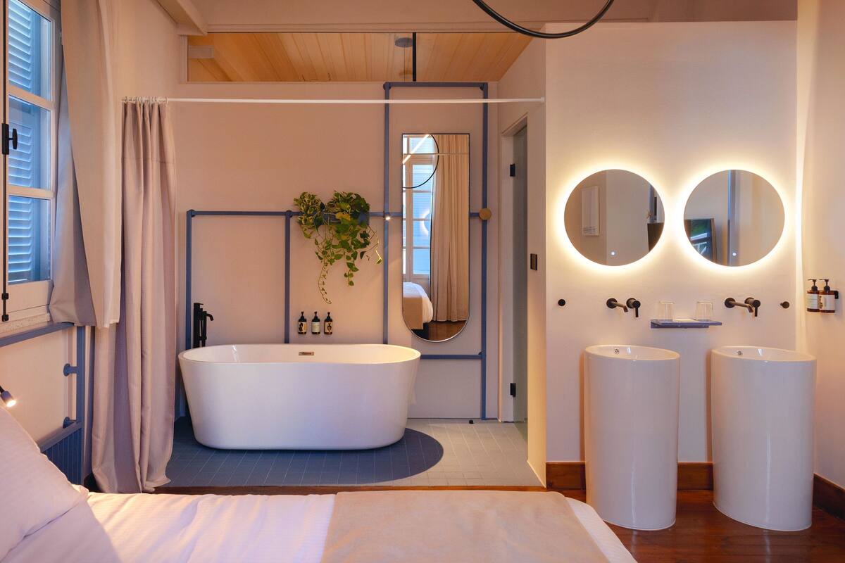 A modern bathroom with a freestanding bathtub, two round mirrors, and a plant.