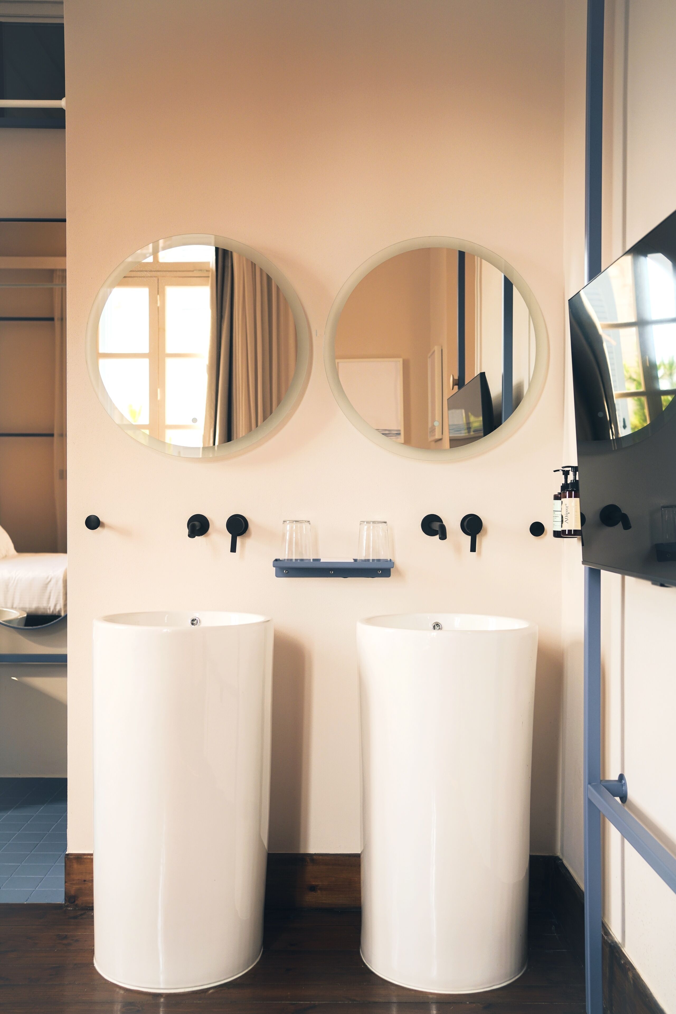 Een badkamer met twee grote witte wastafels, een ronde spiegel boven elke wastafel, en een plank met een glas en een fles.