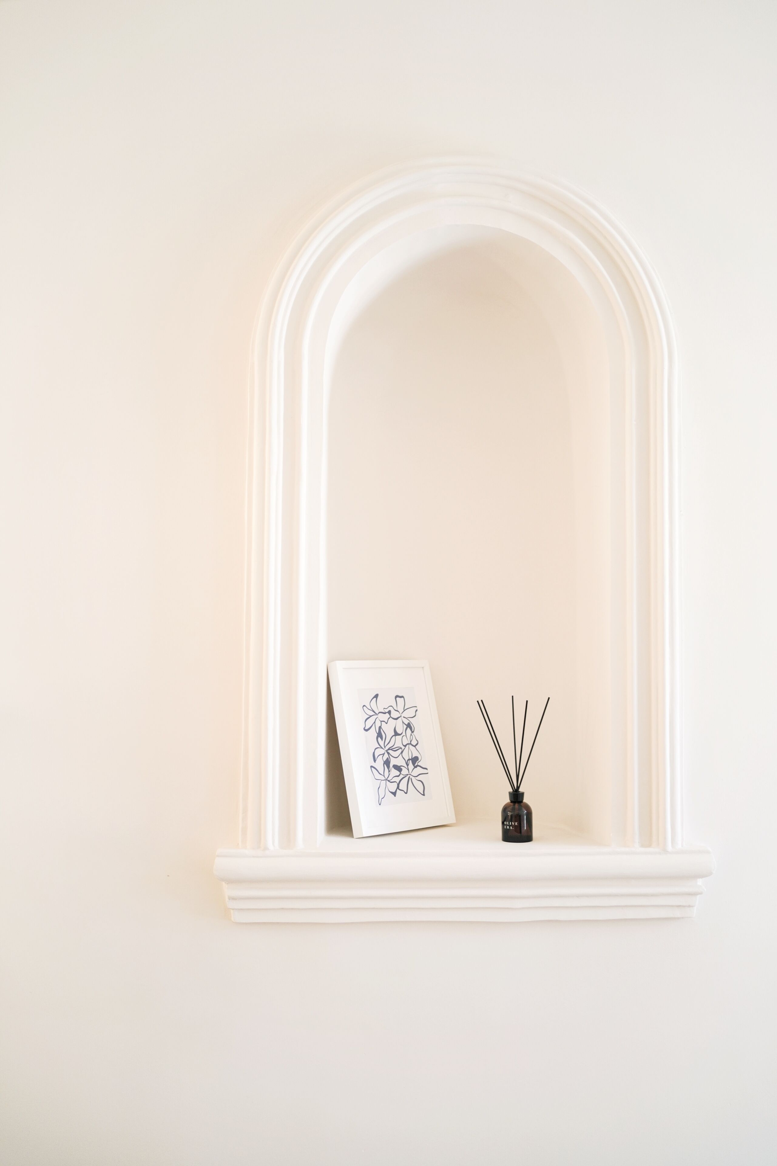 A white mantelpiece with a framed picture and a small black bottle of reed diffuser.