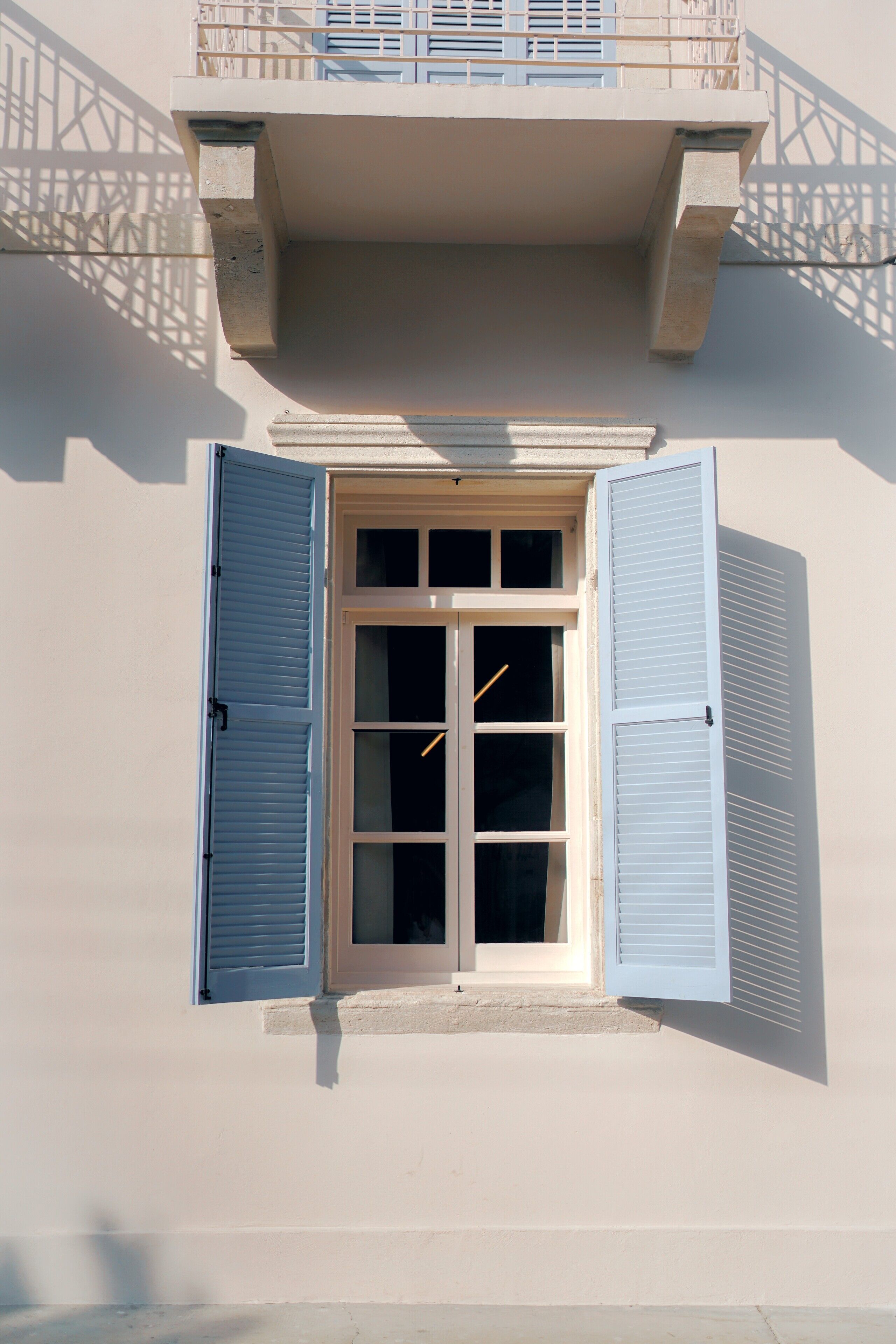 A building with a window featuring blue shutters, a balcony with a railing, and a concrete structure above the window.
