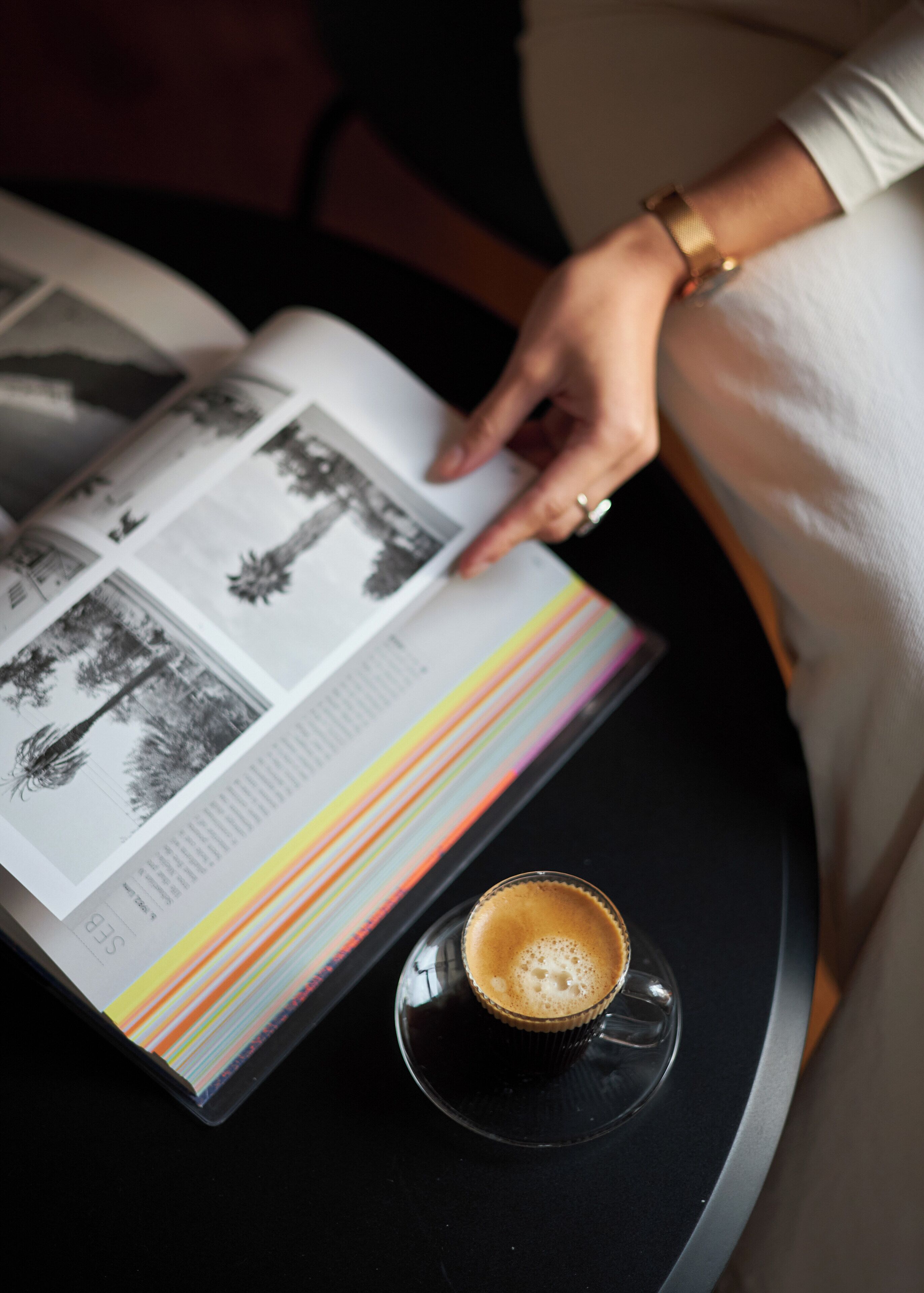 Una persona leyendo un libro con una taza de café sobre una mesa.