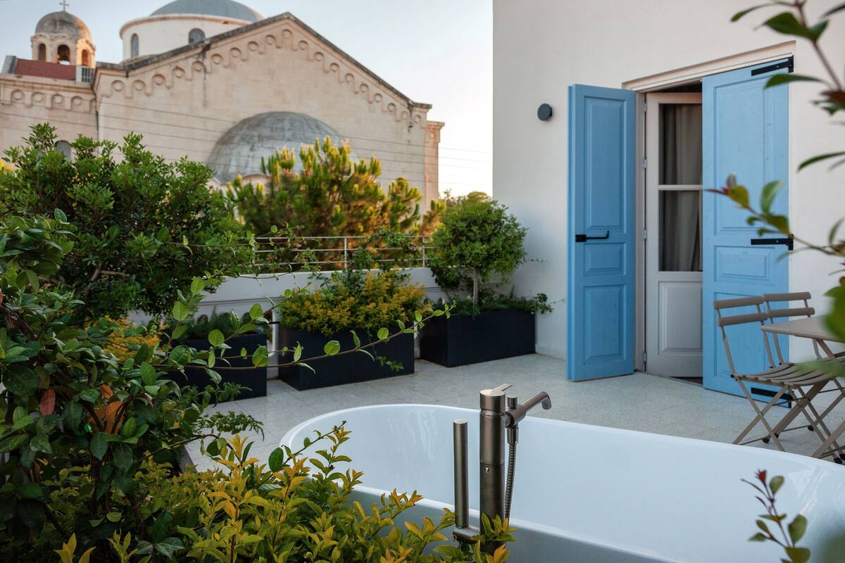A rooftop terrace with a bathtub, blue doors, and a building with domed architecture in the background.