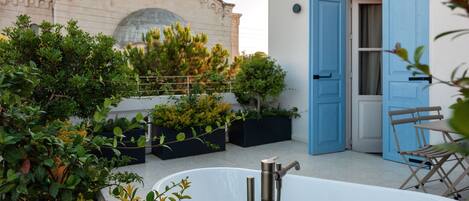 A rooftop terrace with a bathtub, blue doors, and a building with domed architecture in the background.