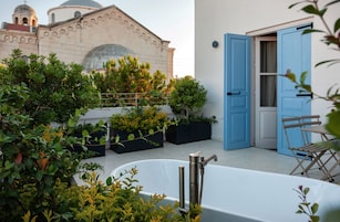 Terraço no telhado com banheira, portas azuis e um edifício com arquitetura em cúpula ao fundo.