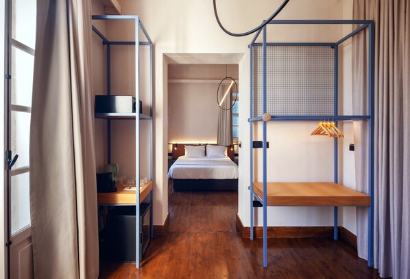 A compact hotel room with a bunk bed, a desk with a chair, a small table, and a hanging light fixture.