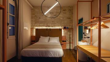 A bedroom with a large bed, a hanging circular light fixture, a stone wall, and a wooden bench.