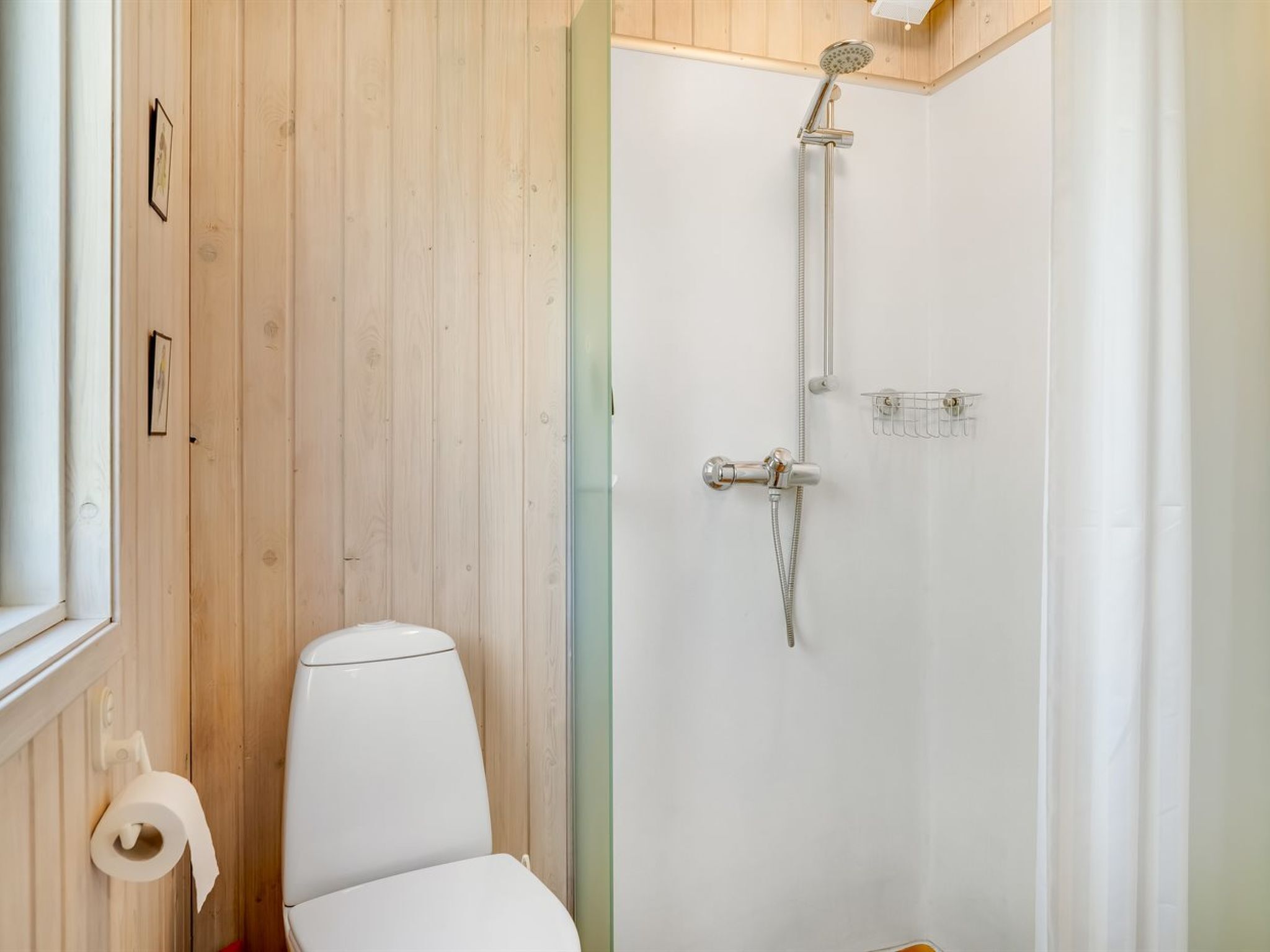 A bathroom with a wooden panel wall, a white toilet, a shower with a handheld showerhead, and a towel rack.