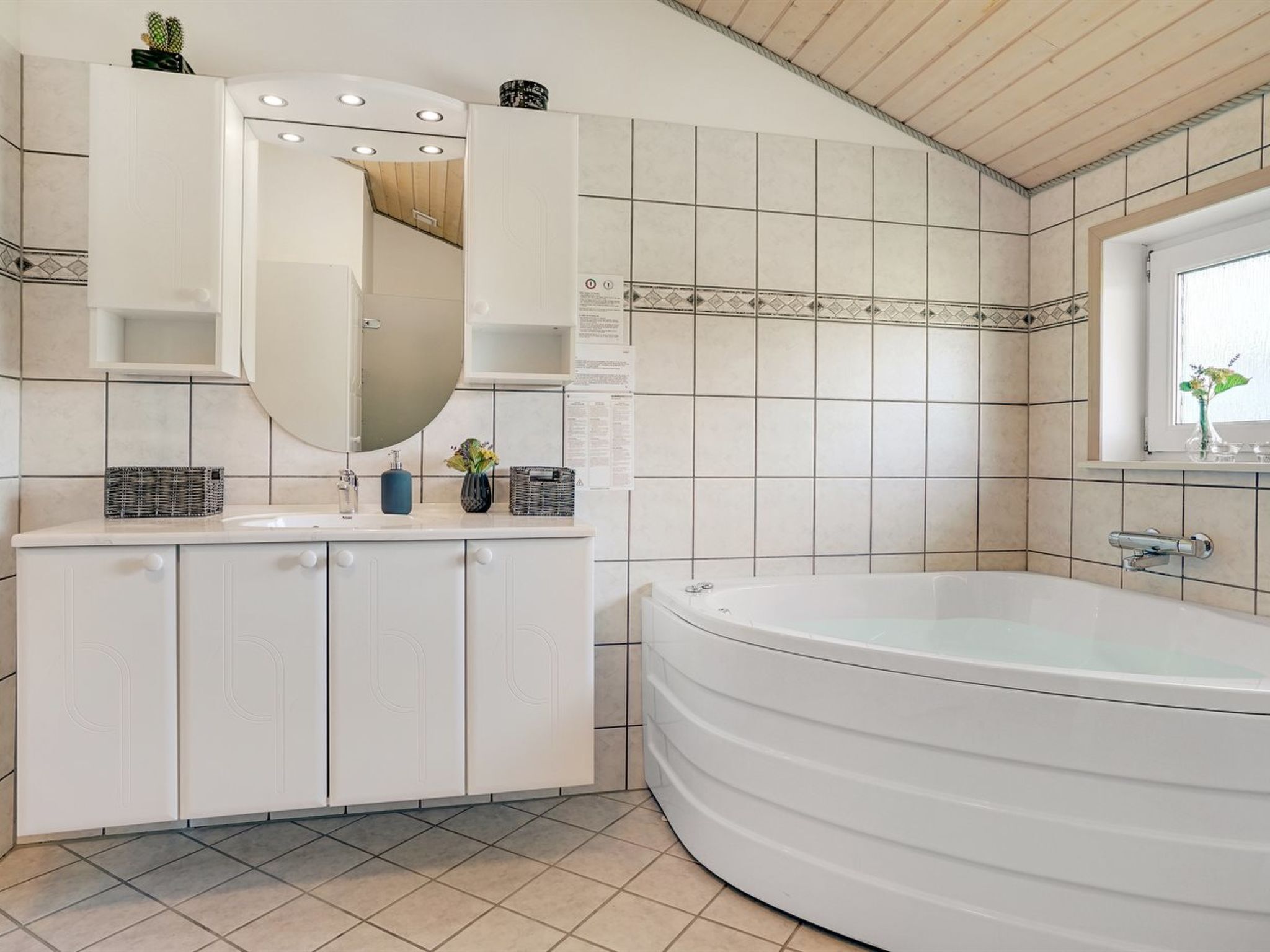 A modern bathroom with a freestanding bathtub, a large mirror, and a vanity with storage baskets.