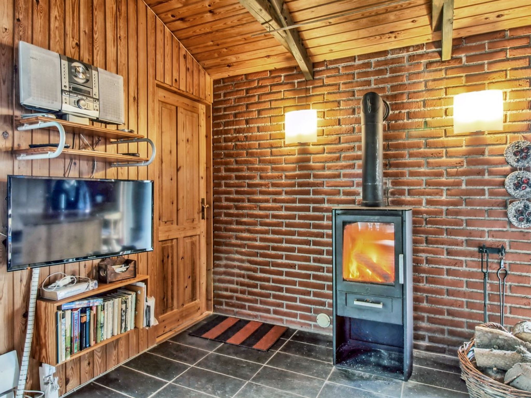 Une pièce chaleureuse avec un mur en briques, un poêle à bois, une télévision et une bibliothèque.