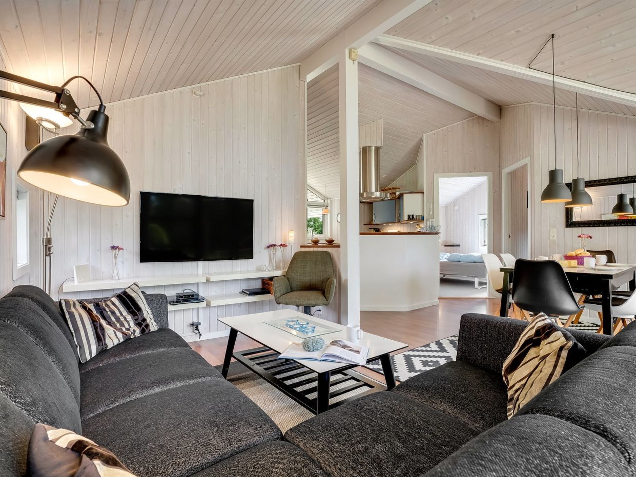 A modern living room with a large flat-screen TV, a sofa, a coffee table, and a dining area with a table and chairs.
