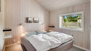 Makuuhuone, jossa on sänky, puuseinät, ikkuna ja kaksi seinälle kiinnitettyä hyllyä, joilla on valokuvia.