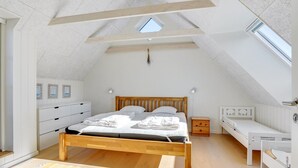 Een slaapkamer met een schuine plafond, een houten bed, een nachtkastje en een klein bureau.
