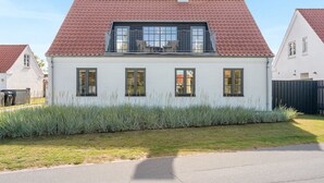 Een tweelaags huis met een rode pannendak, een balkon met metalen hekwerk en een verzorgd gazon.
