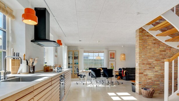 Een moderne keuken met een centraal eiland, een eetgedeelte met stoelen, en een trap bij een bakstenen muur.