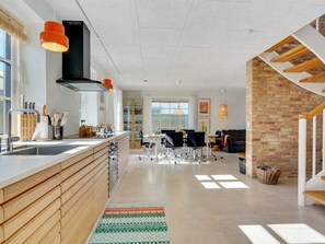 Une cuisine moderne dotée d’un îlot central, d’un coin repas avec des chaises et d’un escalier avec un mur en briques.