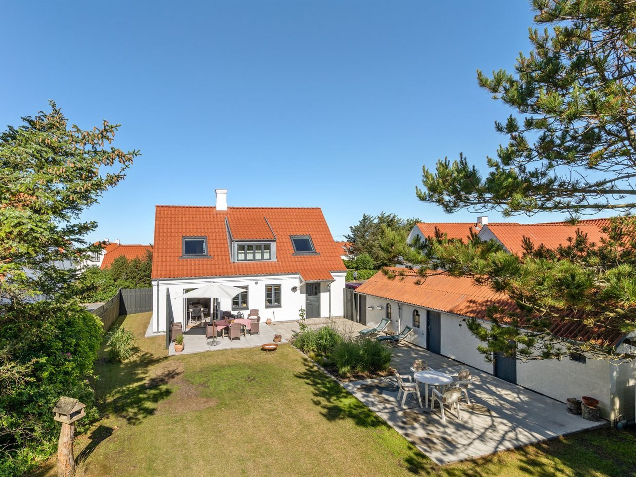 Ein zweistöckiges Haus mit rotem Ziegeldach, einer überdachten Terrasse mit Gartenmöbeln und einem gepflegten Rasen.