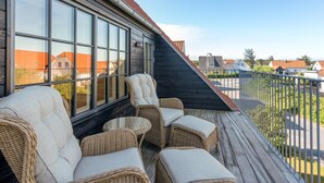 Een balkon met rieten meubels en grote ramen met uitzicht op een woonwijk.