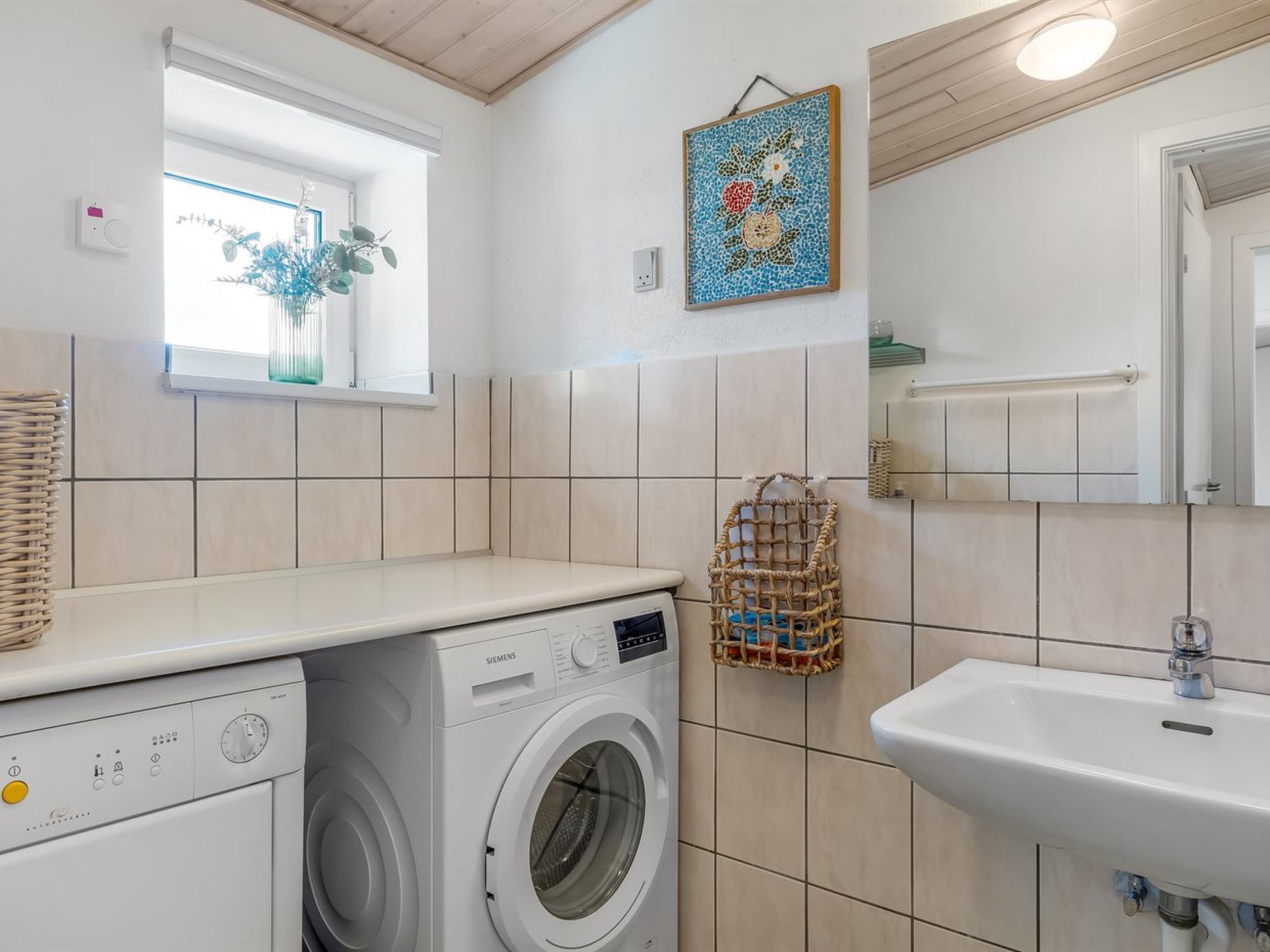Ein kleiner Waschbereich mit Waschmaschine, Spüle und einem Fenster mit Pflanze.