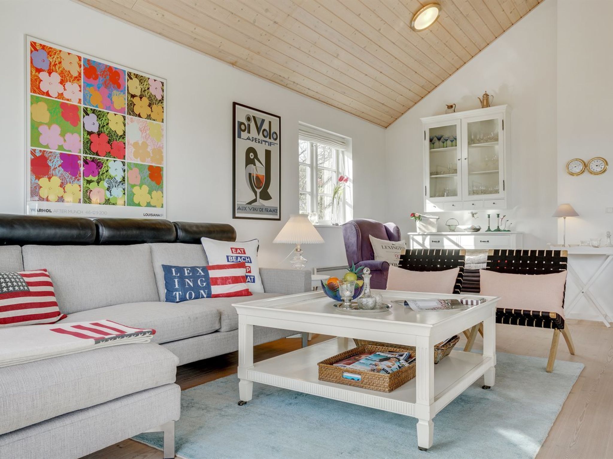 A living room with a sofa, coffee table, and a cabinet. There are posters on the wall and a window with curtains.