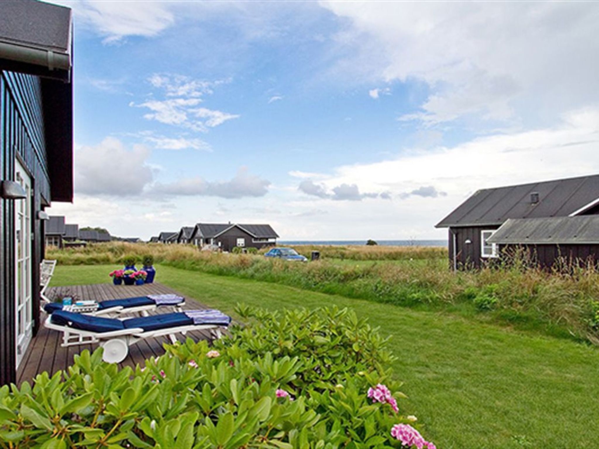 Vue d’une propriété située en bord de mer, avec une terrasse en bois, des chaises longues et une pelouse verdoyante.