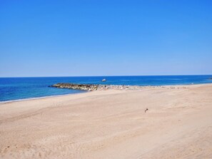 Une vaste plage de sable bordée d’un brise-lames rocheux et baignée d’eaux bleues et calmes.