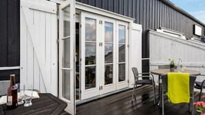A wooden deck with a white door leading to a room, a table with chairs, and a bottle of beer. - "Tofan" - 100m to the fjord by Interhome (Vestervig)