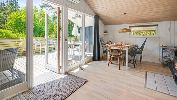 Une pièce chaleureuse avec un plafond en bois, une table à manger avec des chaises, une cheminée et une grande porte-fenêtre coulissante donnant sur une terrasse extérieure.