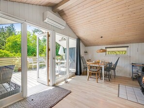 Ein gemütliches Zimmer mit Holzbalkendecke, einem Esstisch mit Stühlen, einem Kamin und einer großen Schiebeglastür, die auf eine Terrasse im Freien führt.
