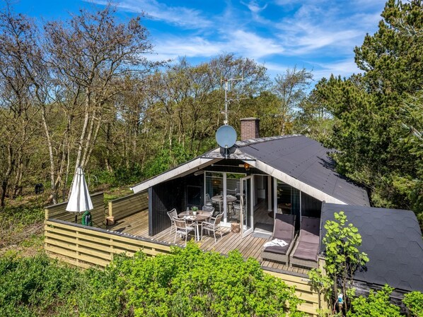 Eine moderne Holzhütte mit Terrasse, Sitzgelegenheiten im Freien und einer Satellitenschüssel.