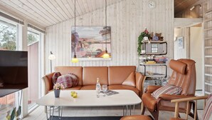 En moderne stue med et hvidt bord, lædersofa og lænestol, træpaneler og et stort vindue.
